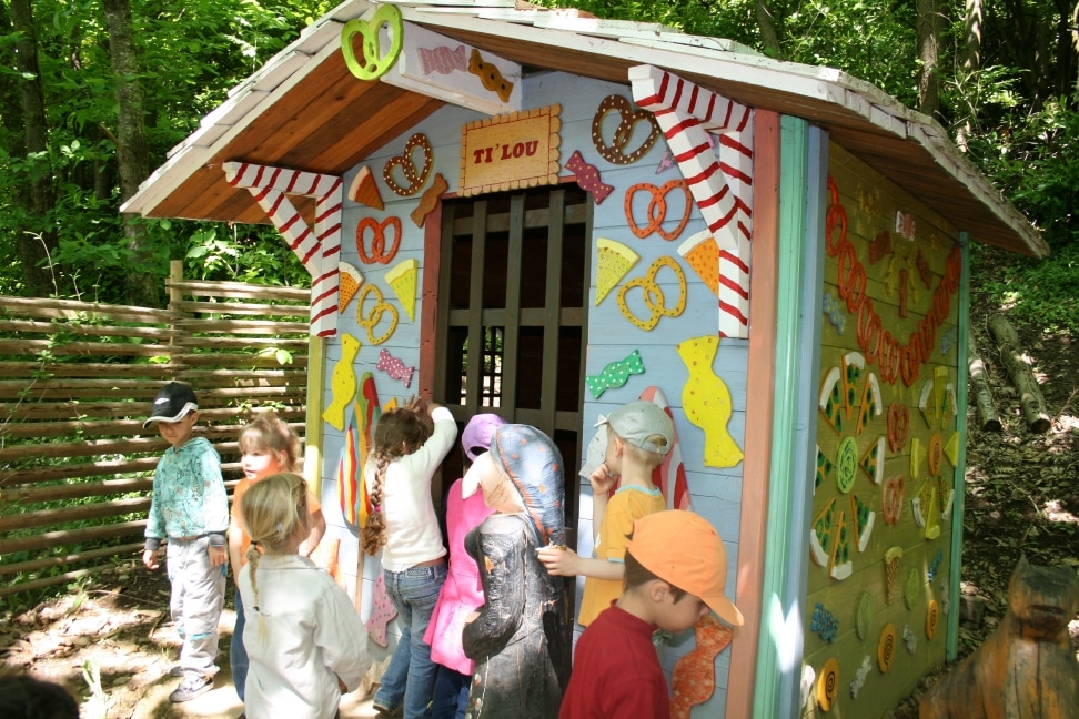 Enfants curieux devant la maison Ti' Lou décorée de bonbons et bretzels géants en bois.